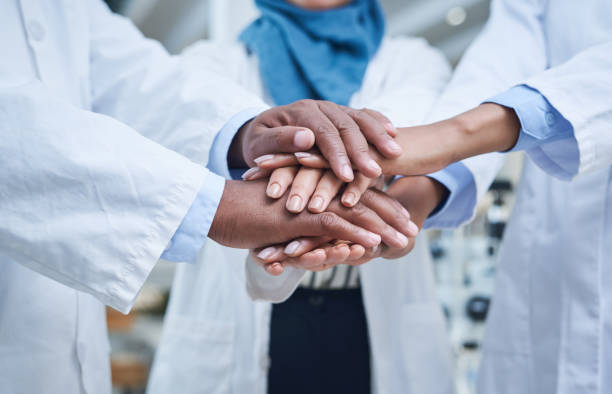 Shot of a group of unrecognisable scientists joining hands in solidarity in a laboratory